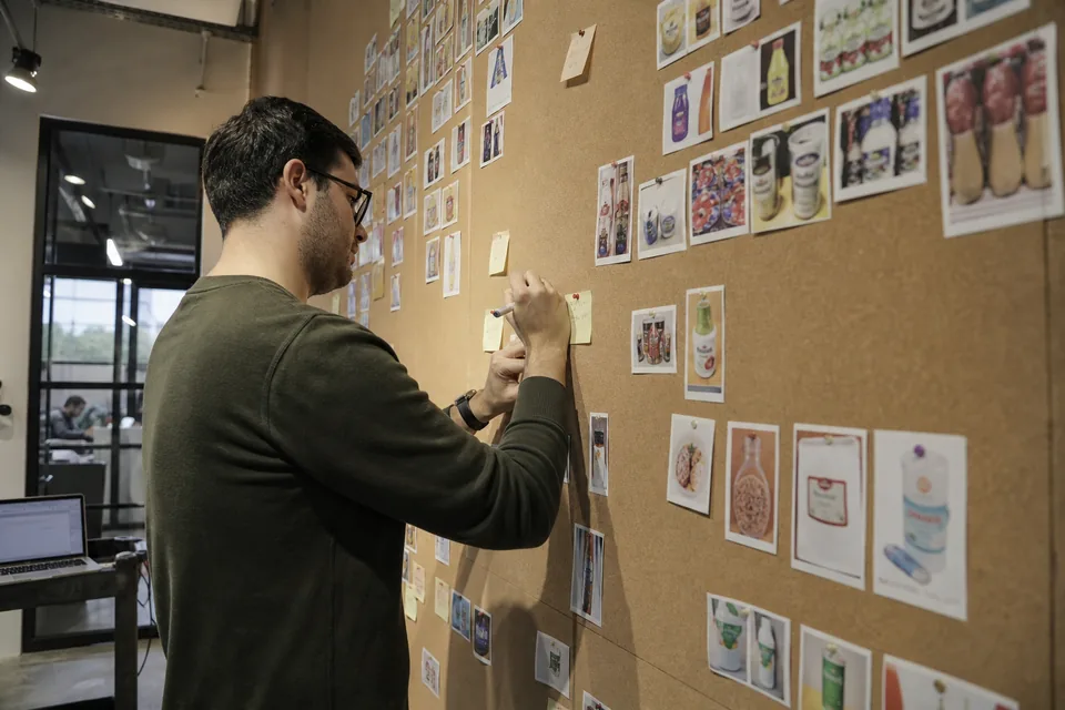Engineer looking at a wall of printed sample images pinned in rows by class in a small lab