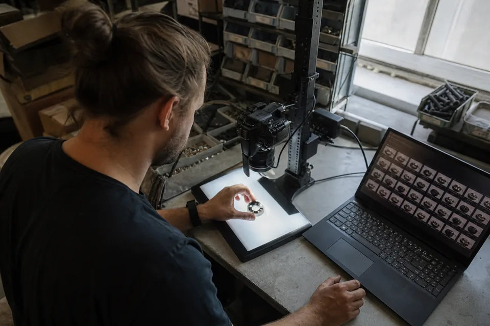 Person photographing parts on a light table for a dataset, camera on a copy stand and a laptop with the image grid