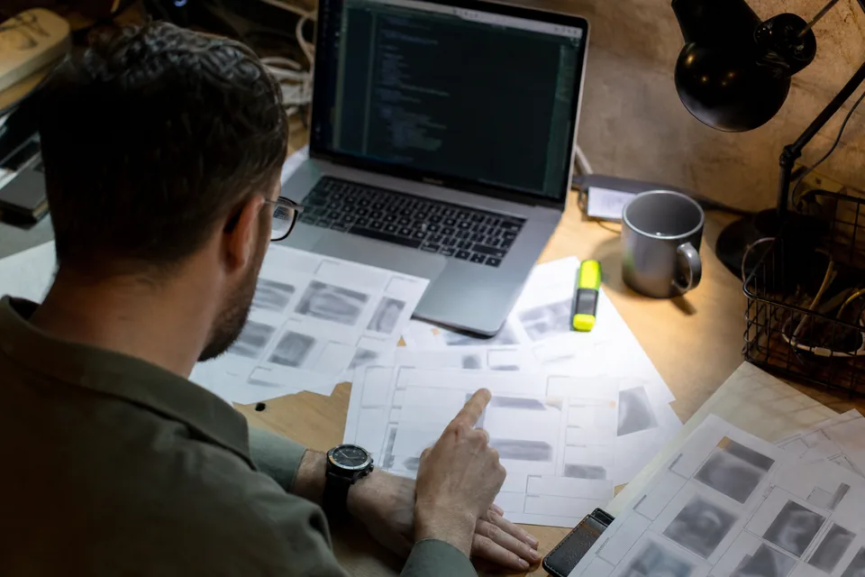 Engineer comparing printed dataset annotation files spread on a desk next to a laptop